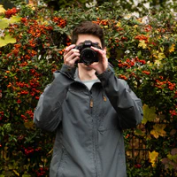 Avatar for Tobi: Young man standing in front of a red flowering bush and holding a camera to his face